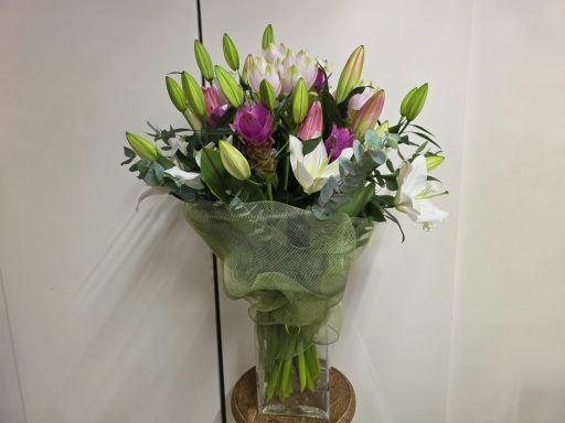 Bouquet of mixed flowers, including lilies and purple blooms, wrapped in green paper.