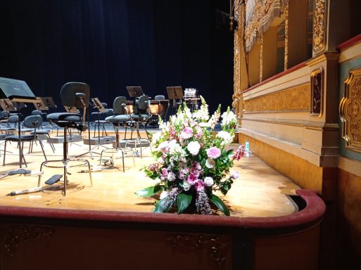 Bouquet of flowers in front of a stage with musical instruments and chairs.