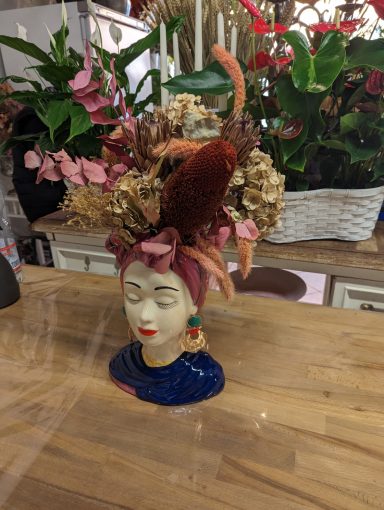 Ceramic head vase adorned with flowers and a colorful bird on a wooden table.