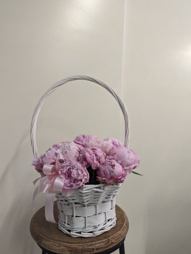 Cesto bianco con peonie rosa in un ambiente luminoso.