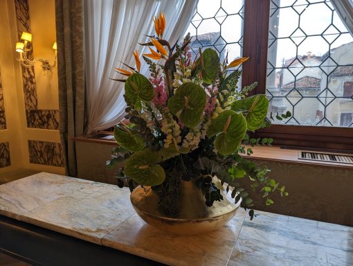 Vibrant floral arrangement in a vase on a marble surface, with a window backdrop.