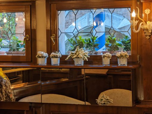 Interni di un ristorante con vasi di fiori bianchi e finestre decorative.