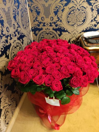 Bouquet of red roses arranged with greenery and tied with a decorative ribbon.