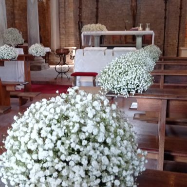 Fiori bianchi di gypsophila decorano una chiesa con panche in legno.
