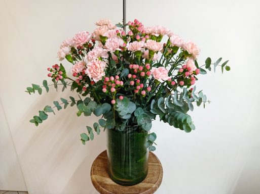 Un vaso di fiori rosa con foglie verdi, decorato su uno sfondo chiaro.