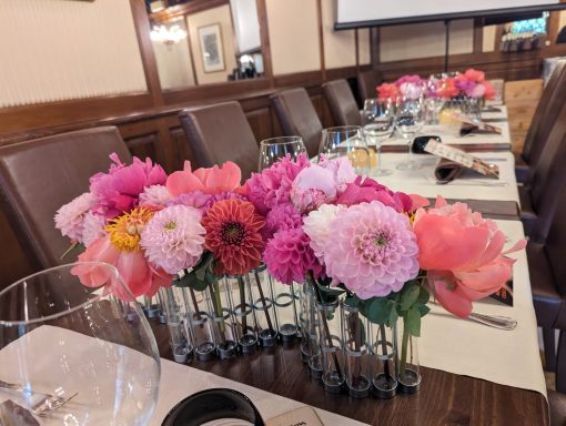 Vibrant pink and purple flowers arranged in small vases along a dining table.