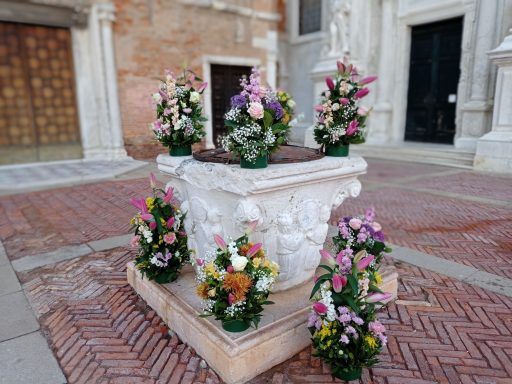 Fountain adorned with colorful flowers, located in a brick courtyard.