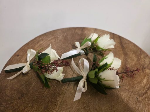 Boutonnières with white roses and greenery tied with ribbons on a wooden surface.