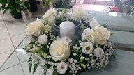 Corona di fiori bianchi con una candela centrale, decorata con foglie verdi.