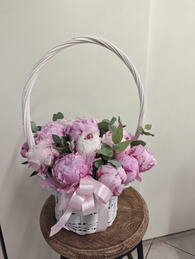 Vibrant pink peonies arranged in a woven basket with a ribbon.