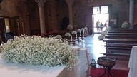 Interno di una chiesa decorata con fiori bianchi e panchine in legno.
