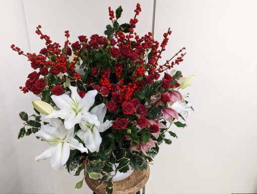 Bouquet of red roses, white lilies, and greenery in a decorative vase.