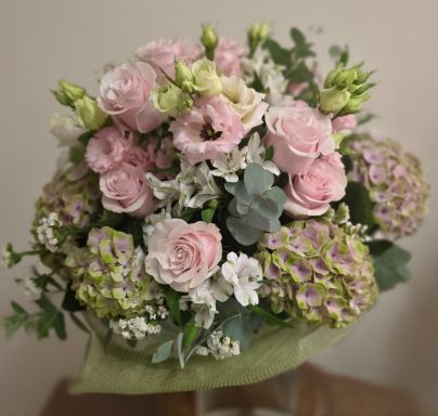 Bouquet of pink roses, white flowers, and green accents in a soft arrangement.