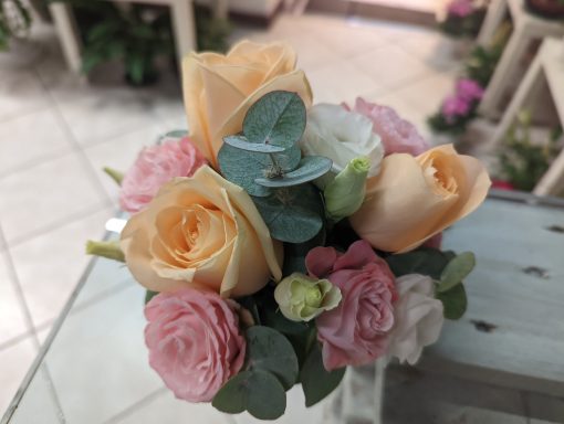 Bouquet of soft pink and peach roses with green leaves arranged elegantly.