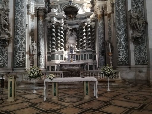 Interno di una chiesa con altare decorato e statue su sfondo ornato.